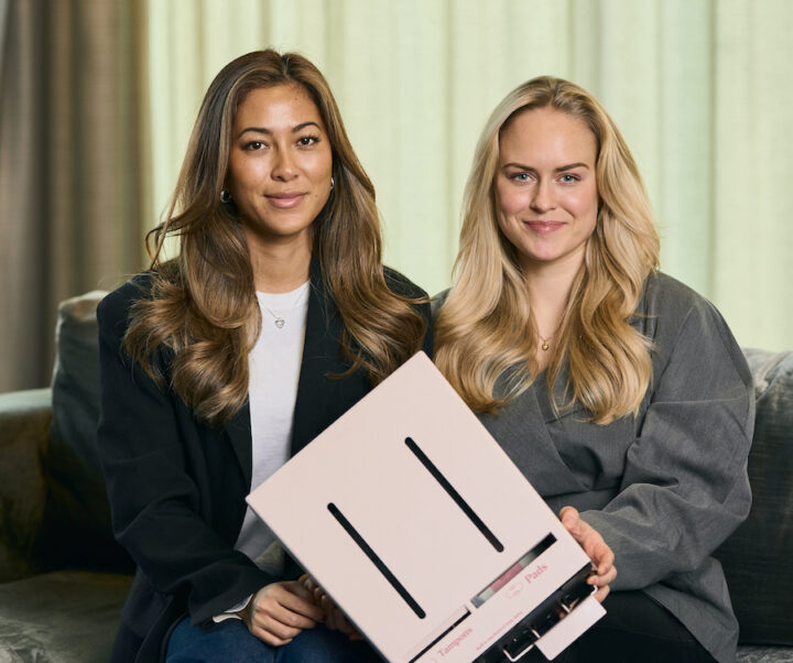 Herbox grundare Hanna och Linn poserar tillsammans med en rosa mensskyddsautomat i en varm och modern miljö