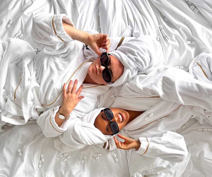 Två kvinnor i badrock på hotellbädd omgivna av Herbox-produkter.