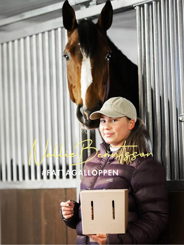 Nellie Berntsson i ridkläder står bredvid en häst i en stallmiljö, håller en Herbox för tamponger. Text i bilden: "Nellie Berntsson #FATTAGALOPPEN".