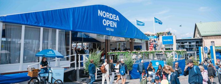 Folksamling vid Nordea Open Båstad, med tält och blå skyltar i bakgrunden. Herbox sponsrar eventet med fria mensskydd.