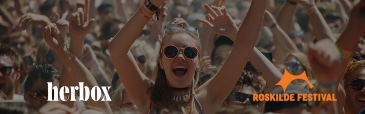 En publik från en festival, med en glad person i mitten som lyfter armarna i luften. logotyper: "herbox" och "Roskilde Festival".