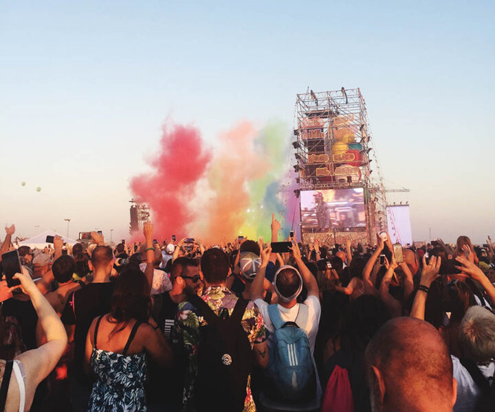 Folkfest med publik framför stor scen, färgade rökpuffar i bakgrunden.